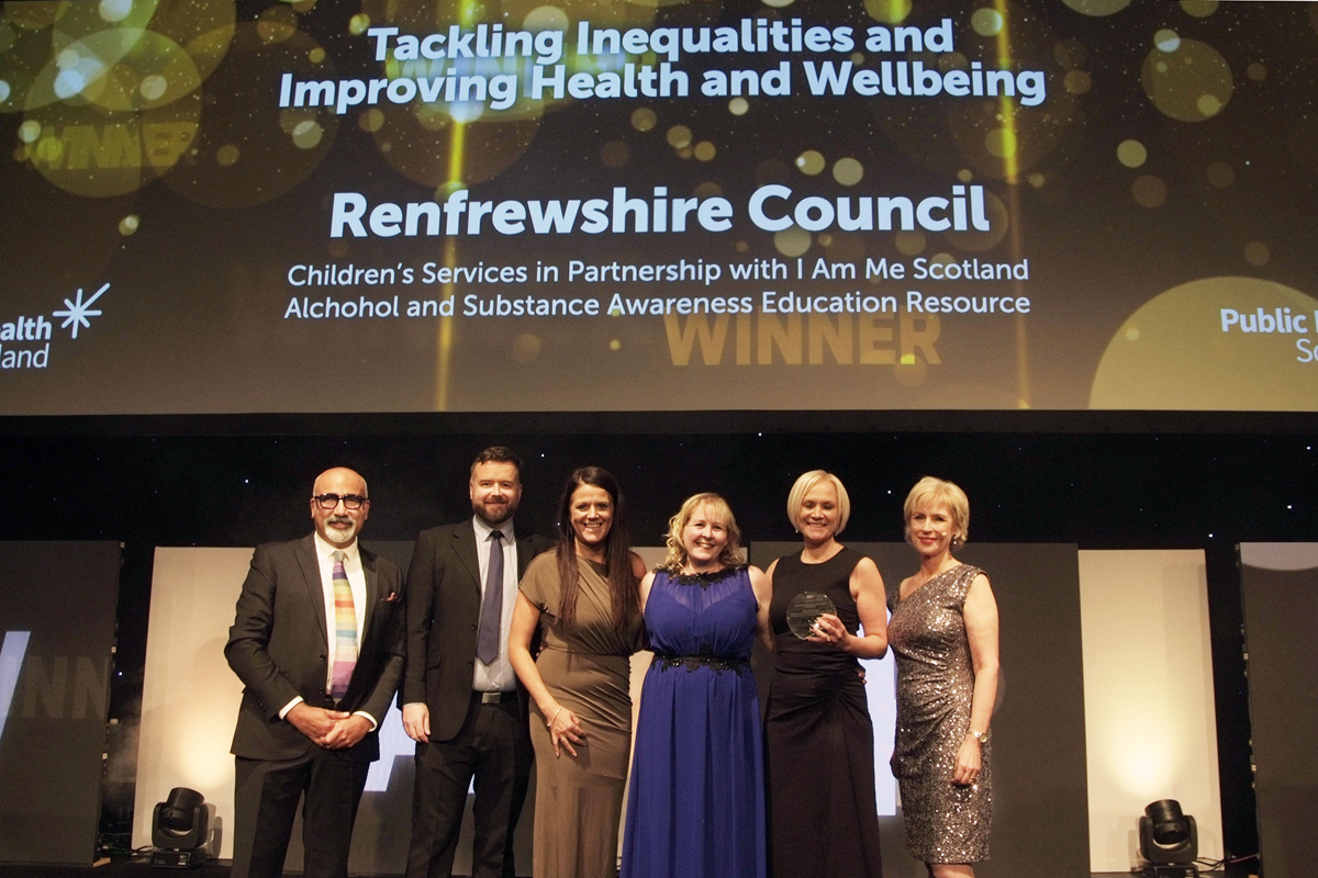 A group of people smiling, collecting an award on stage.