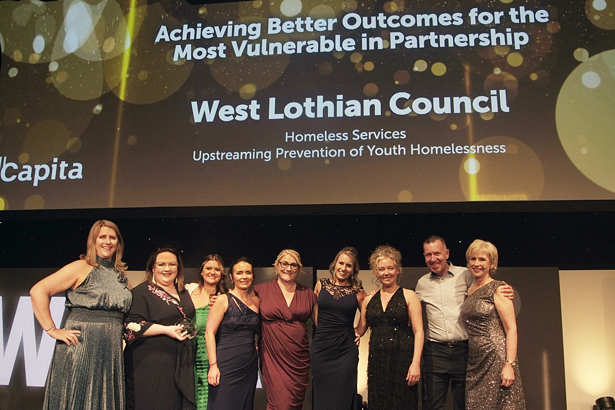 A group of people smiling, collecting an award on stage.