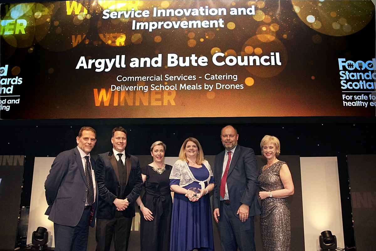 A group of people smiling, collecting an award on stage.