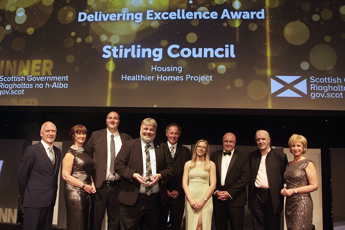 A group of people smiling, collecting an award on stage.