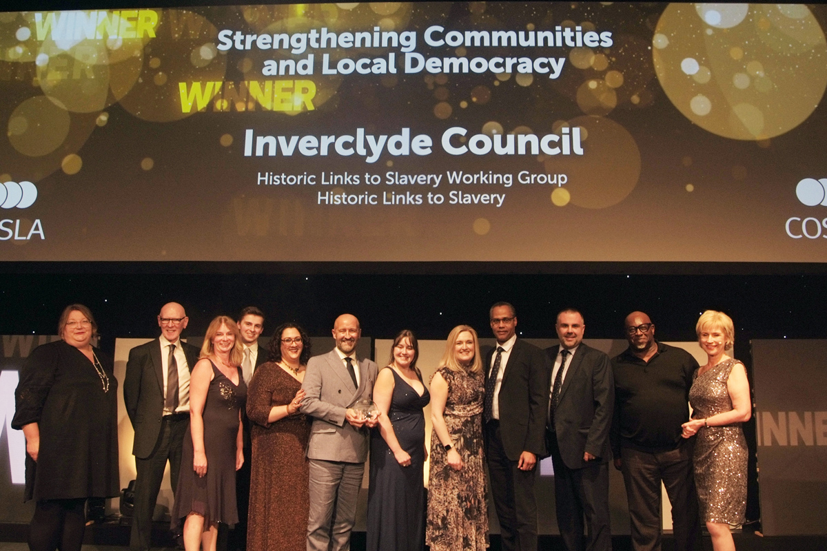 A group of people smiling, collecting an award on stage.