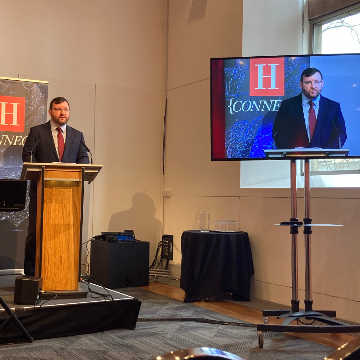 A person presenting to an audience at a lectern.